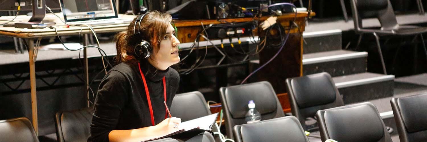 Director, wearing headphones, taking notes in front of a sound desk