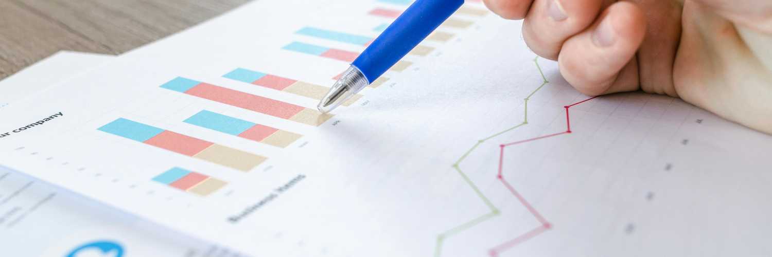 A close-up picture of a person's hand reviewing graphs and spreadsheets